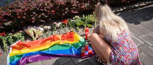 Eine Frau an einer Gedenkstelle mit Blumen, Kerzen und einer Regenbogenflagge in Solingen.
