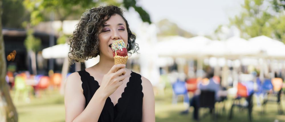 Eine Frau steht auf einer Wiese vor einem Festzelt und isst ein Eis.