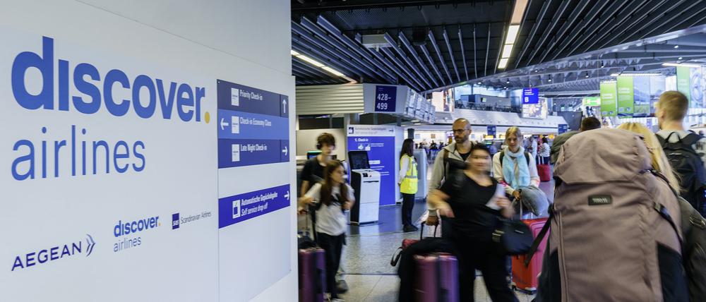 Reisende gehen am Frankfurter Flughafen zum Check-in an den Schaltern von Discover Airlines vorbei. 