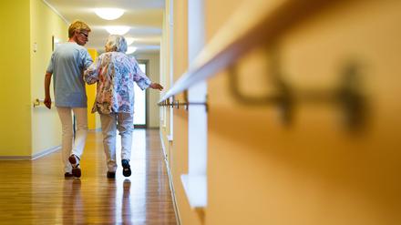 Eine Pflegekraft geht in einem Pflegeheim mit einer älteren Dame über einen Korridor.