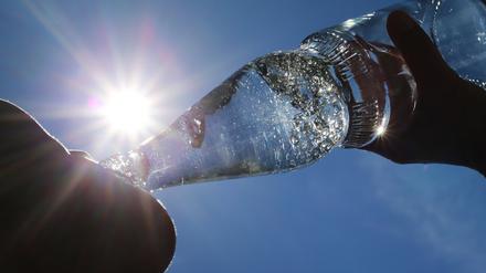 Eine Frau trinkt im Sonnenschein aus einer Flasche sprudelndes Mineralwasser. 