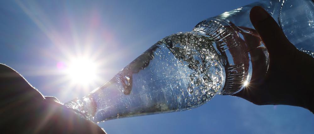 Eine Frau trinkt im Sonnenschein aus einer Flasche sprudelndes Mineralwasser.