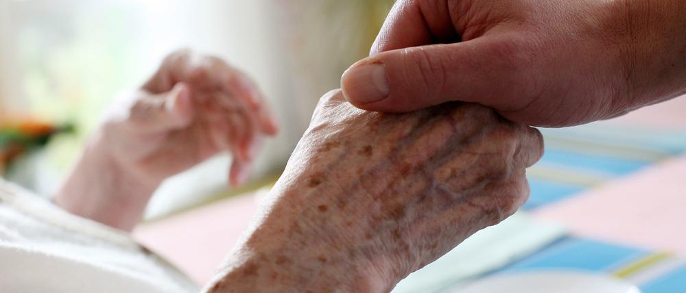 Die Hand eines Pflegers umfasst die Hand einer Seniorin.