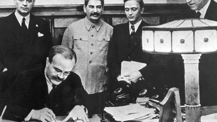 Wjatscheslaw Michailowitsch Molotow, Vorsitzender des UdSSR-Rats, unterzeichnet den Hitler-Stalin-Pakt in Moskau (1939). Hinter ihm: der NS-Außenminister Joachim von Ribbentrop und Josef Stalin.