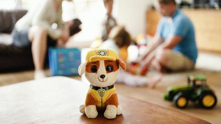 Eine Pflegemutter und -vater sitzen hinter einem Stofftier mit ihren beiden Pflegekindern im Wohnzimmer. Tausende Kinder wachsen in Pflegefamilien auf.