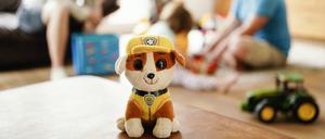 Eine Pflegemutter und -vater sitzen hinter einem Stofftier mit ihren beiden Pflegekindern im Wohnzimmer. Tausende Kinder wachsen in Pflegefamilien auf.