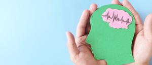 Hände halten einen Pappschnitt eines Kopfes mit Gehirn.