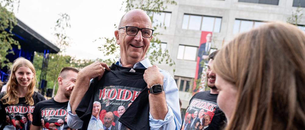 Dietmar Woidke (SPD), Brandenburgs Ministerpräsident, hält auf dem SPD-Sommerfest in Potsdam ein T-Shirt mit Bildern von sich in der Hand.