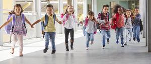 Kinder rennen mit Ranzen auf dem Rücken und Schultüten in den Händen einen Schulkorridor entlang.