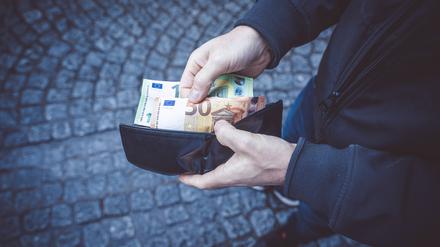 Ein Mann öffnet sein Portemonnaie und hält 150 Euro in Banknoten in der Hand.(Symbolbild)