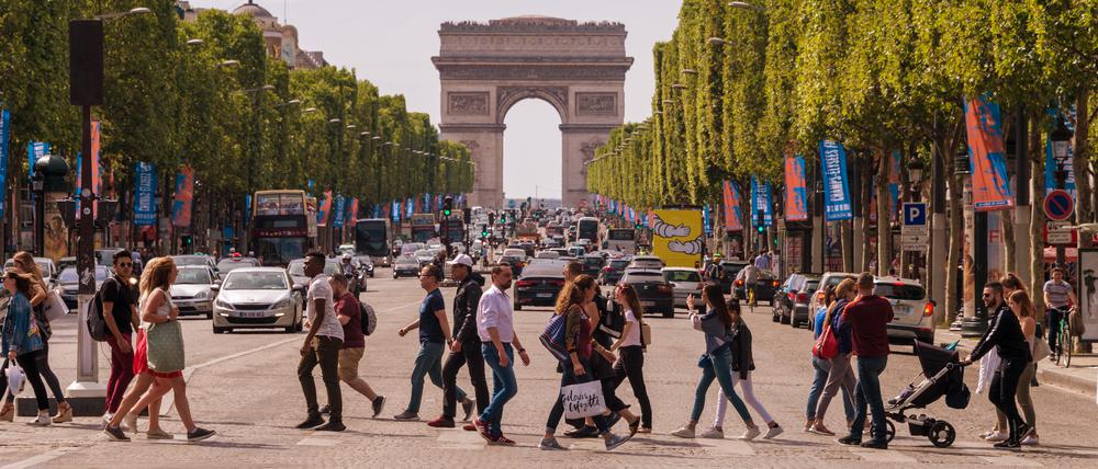 Menschen überqueren die Avenue des Champs-Elysees mit dem Arc de Triomphe im Hintergrund (Symbolbild).