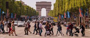 Menschen überqueren die Avenue des Champs-Elysees mit dem Arc de Triomphe im Hintergrund (Symbolbild).