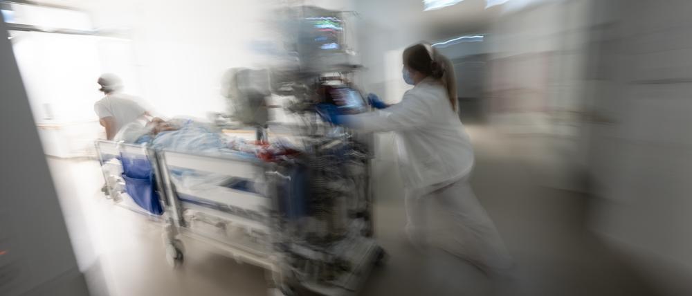 Eine Pflegerin fährt eine Intensivpatientin in einem Krankenbett durch einen Gang einer Klinik.