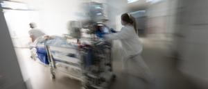 Eine Pflegerin fährt eine Intensivpatientin in einem Krankenbett durch einen Gang einer Klinik.