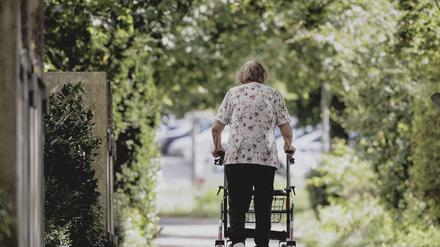 Eine Frau geht mit ihrem Rollator auf einem Weg von der Kamera weg. (Symbolfoto)