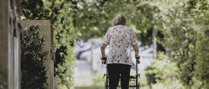 Eine Frau geht mit ihrem Rollator auf einem Weg von der Kamera weg. (Symbolfoto)