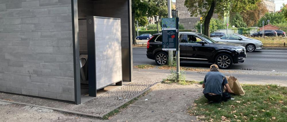 Ein Mann sitzt vor einer Toilettenanlage an der Osloer Straße.