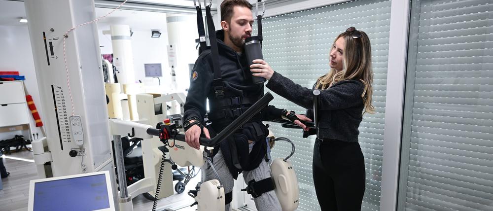 Mike Glemser absolviert in einer Reha eine Übungseinheit bei einer Robotergestützten Gangtherapie. Rechts seine Lebensgefärtin.
