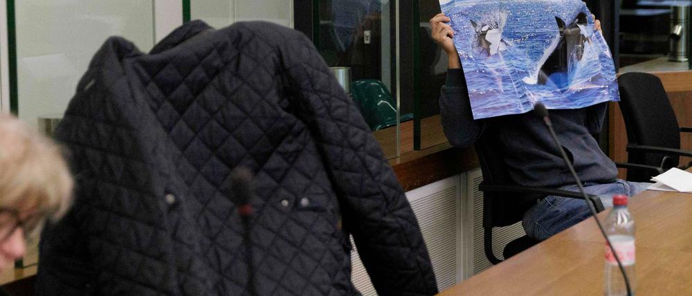 Die beiden Angeklagten verdecken sich hinter einer Jacke und einem Poster beim Prozessauftakt im Berufungsprozess nach einer Serie rechtsextremer Straftaten.