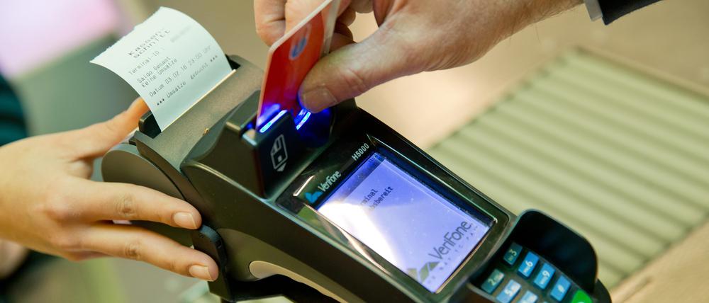 Eine Karte wird an den Bezahl-Terminal an der Kasse eines Supermarktes gehalten.