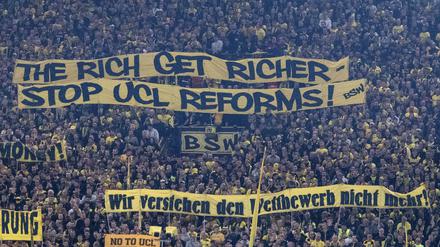 Fans zeigen Banner. Dortmunder Anhänger mit Tarnsparenten mit der Aufschrift „The rich get richer“ („Die Reichen werden reicher“).  