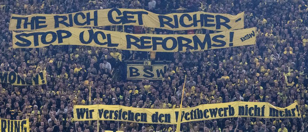 Fans zeigen Banner. Dortmunder Anhänger mit Tarnsparenten mit der Aufschrift „The rich get richer“ („Die Reichen werden reicher“).  