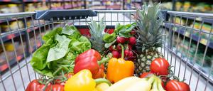Ein Einkaufskorb mit Obst und Gemüse steht in einem Supermarkt. 