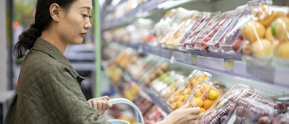 Eine junge Frau steht an einem Kühlregal mit abgepacktem Obst und Gemüse.