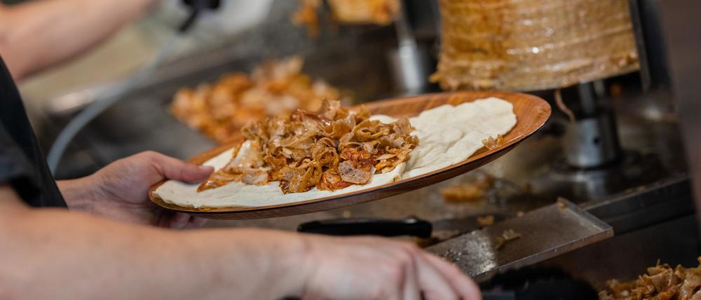 Ein Mitarbeiter einer Dönerbude legt Fleisch auf einen Yufka / Dürüm Döner.