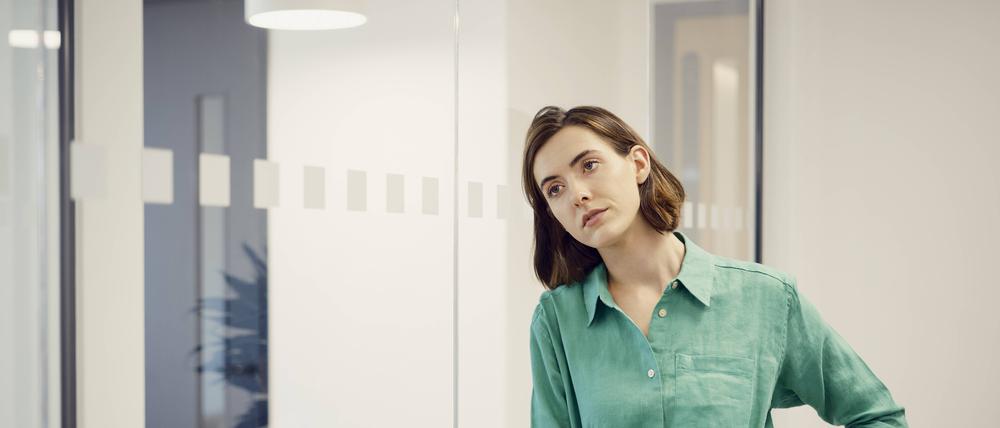 Eine Frau steht in einem Büro und blickt gedankenverloren in die Luft.