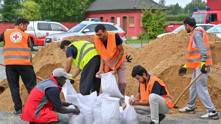 Nach einem Aufruf zur freiwilligen Mithilfe sind Menschen aus einer Unterkunft der Zentralen Ausländerbehörde an Sandsäcken im Einsatz. 