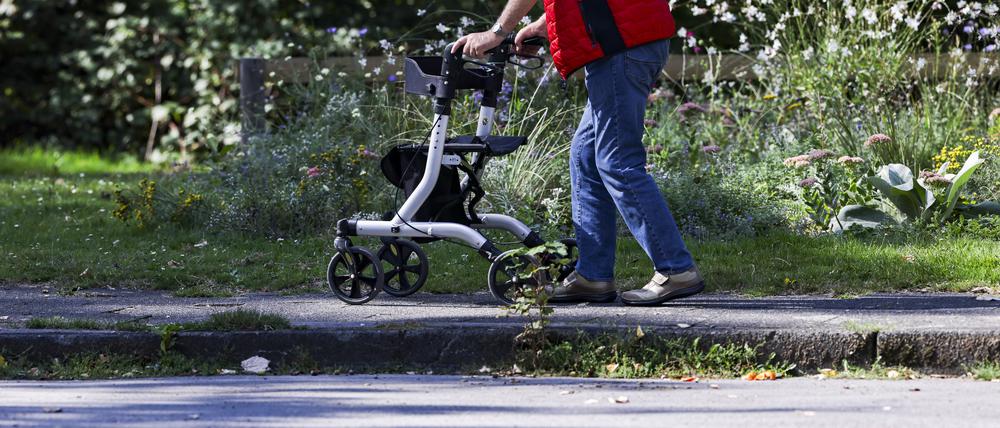 Ein Mann geht mit einem Rollator durch einen kleinen Park. 