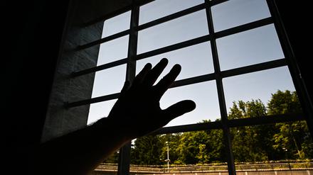 Ein Mann hält in einer Einzelzelle eines Gefängnisses seine Hand ans Fenster (Symbolbild).