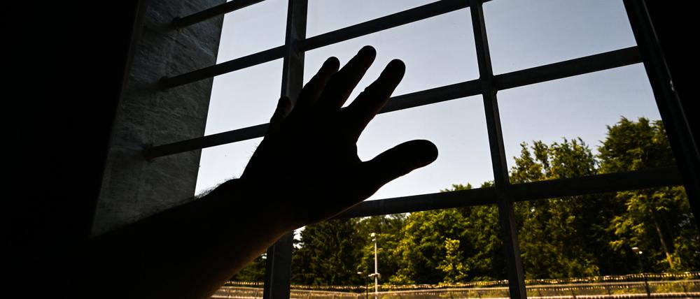 Ein Mann hält in einer Einzelzelle seine Hand ans Fenster.