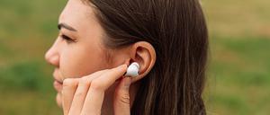 Eine junge Frau setzt sich einen Kopfhörer ins Ohr ein.