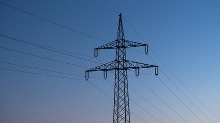 Ein Strommast ist bei Sonnenaufgang als Silhouette zu sehen. (Symbolbild)