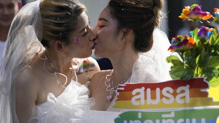 Frauen küssen sich während einer Pride-Parade in Bangkok, während sie ein Plakat zur Unterstützung der Ehegleichheit halten.