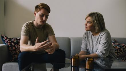 Ein junger Mann sitzt im Gespräch neben seiner Mutter auf einem Sofa.