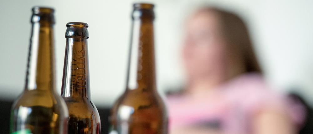 Eine junge Frau sitzt hinter leeren Bierflaschen.