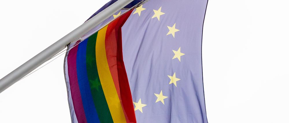 Eine Regenbogenfahne weht neben der EU-Flagge im Wind.