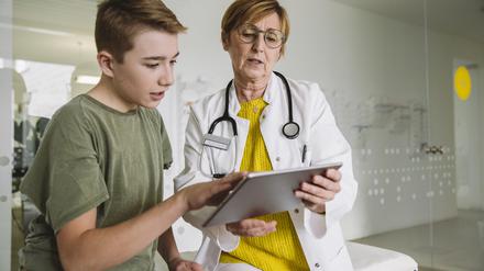 Eine Ärztin schaut mit einem Jungen auf ein Tablet.