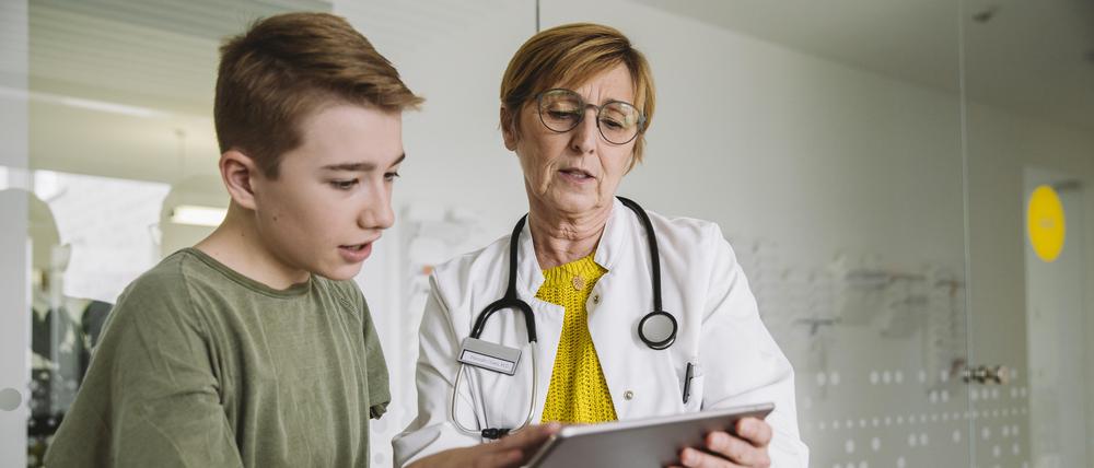 Eine Ärztin schaut mit einem Jungen auf ein Tablet.
