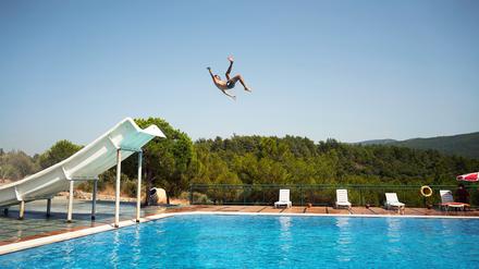 Ein Mann springt in einem Freibad von der Rutsche.