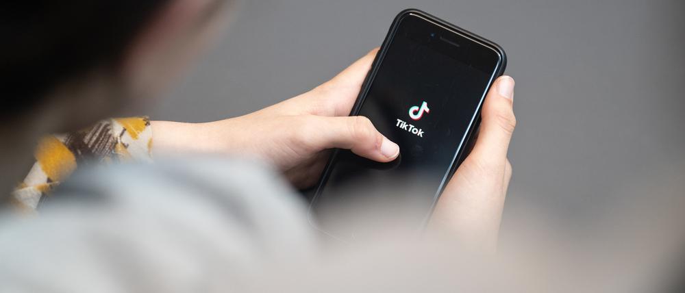 Eine Jugendliche schaut auf ein Smartphone mit angezeigtem TikTok-Logo.  