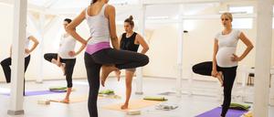 Eine Trainerin übt mit einer Gruppe schwangeren Frauen den Yoga-Stand auf einem Bein. 