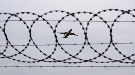 Ein Flugzeug startet – fotografiert durch Stacheldraht am Flughafenzaun. 