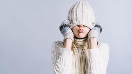 Eine frierende Frau mit Pullover, Mütze und Handschuhen.