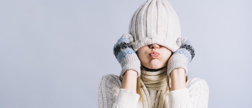 Eine frierende Frau mit Pullover, Mütze und Handschuhen.