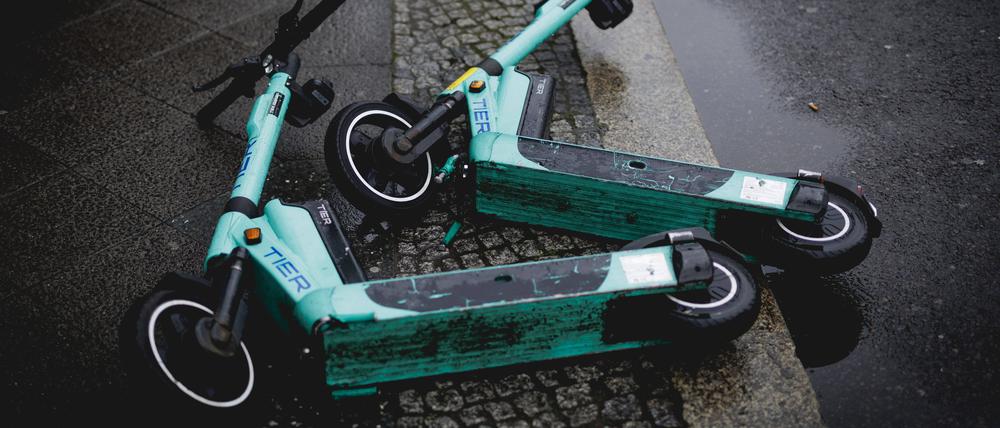 Zwei E-Scooter liegen auf der Straße im Regen.