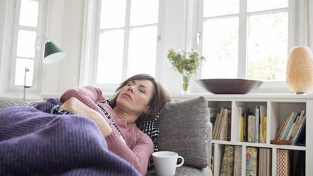 Eine Frau liegt mit Regelschmerzen auf der Couch.